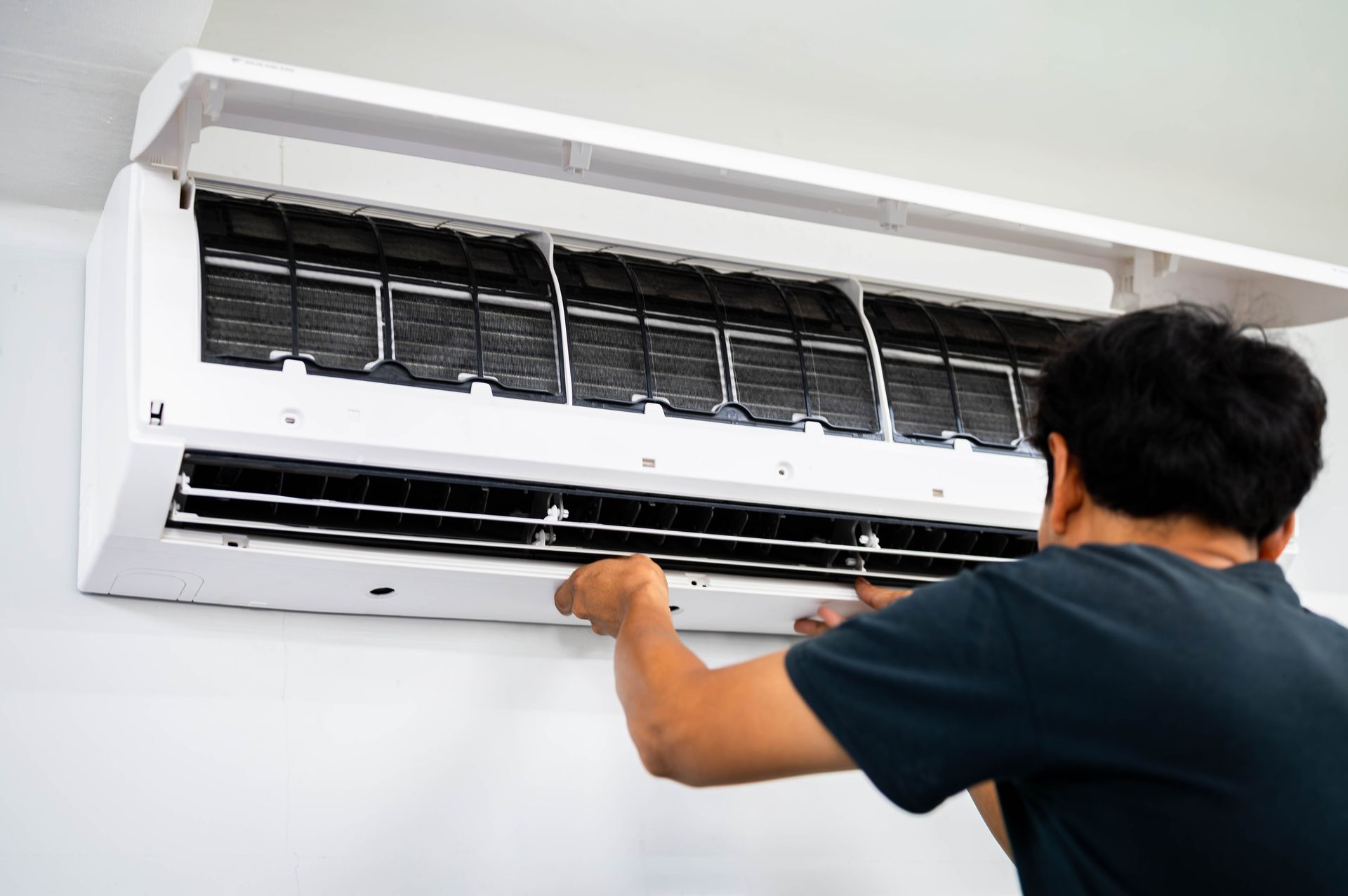 Technician cleaning a wall-mounted air conditioner with the front cover open