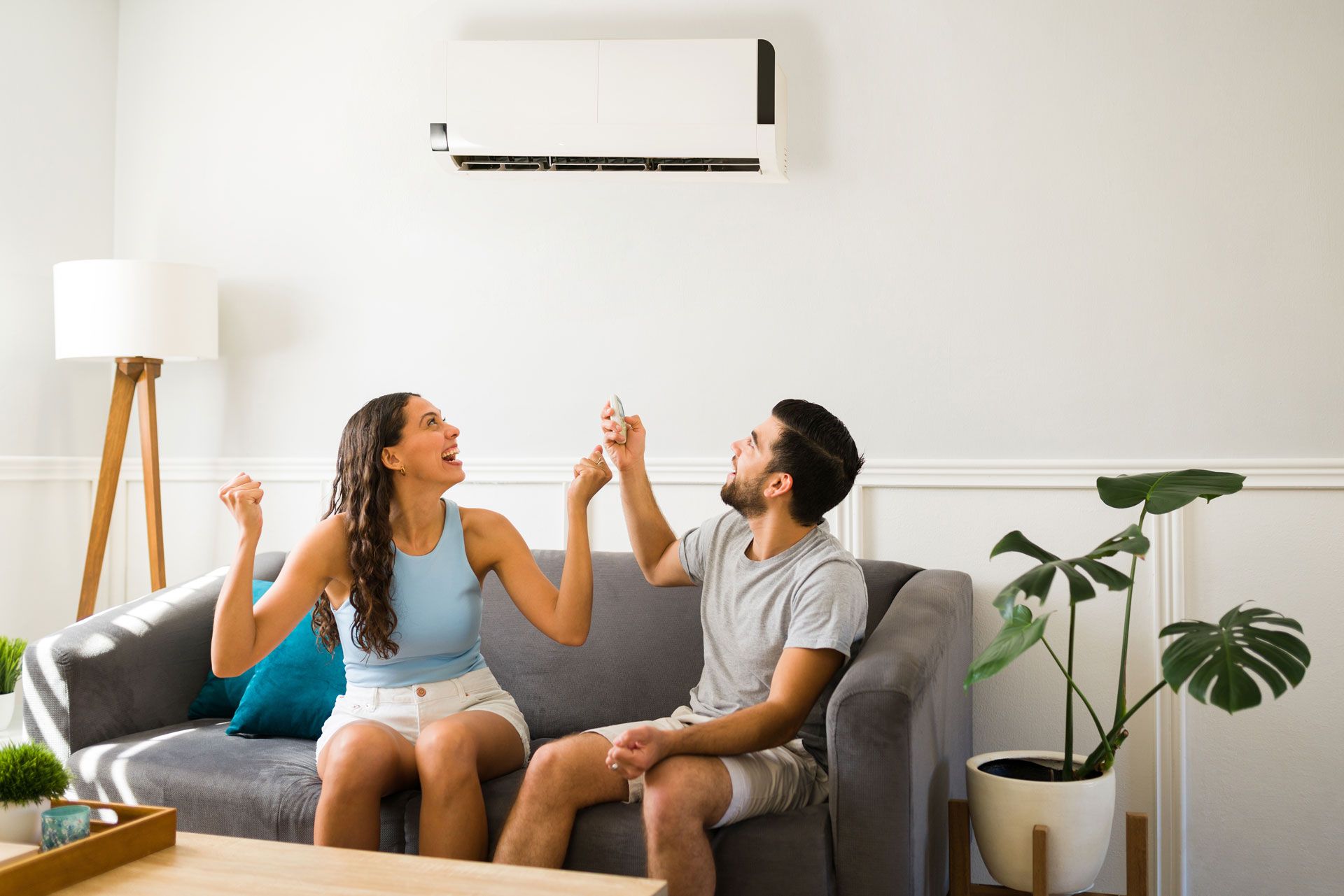 Two people on a couch high-five in a bright living room with a wall-mounted air conditioner.