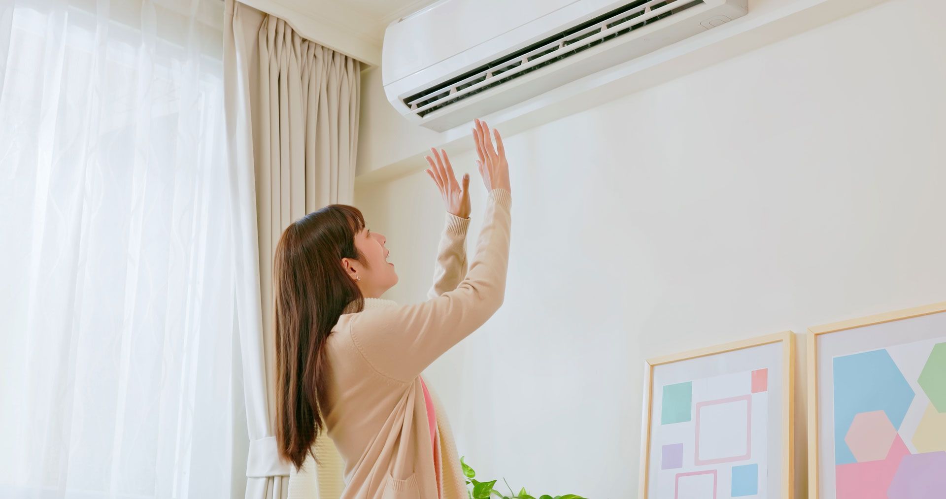 Woman adjusting a wall-mounted air conditioner in a bright room