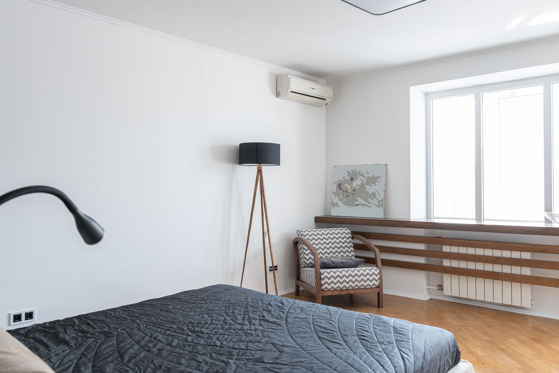 Modern bedroom with a black bed, chair, floor lamp, wall AC, and window with blinds