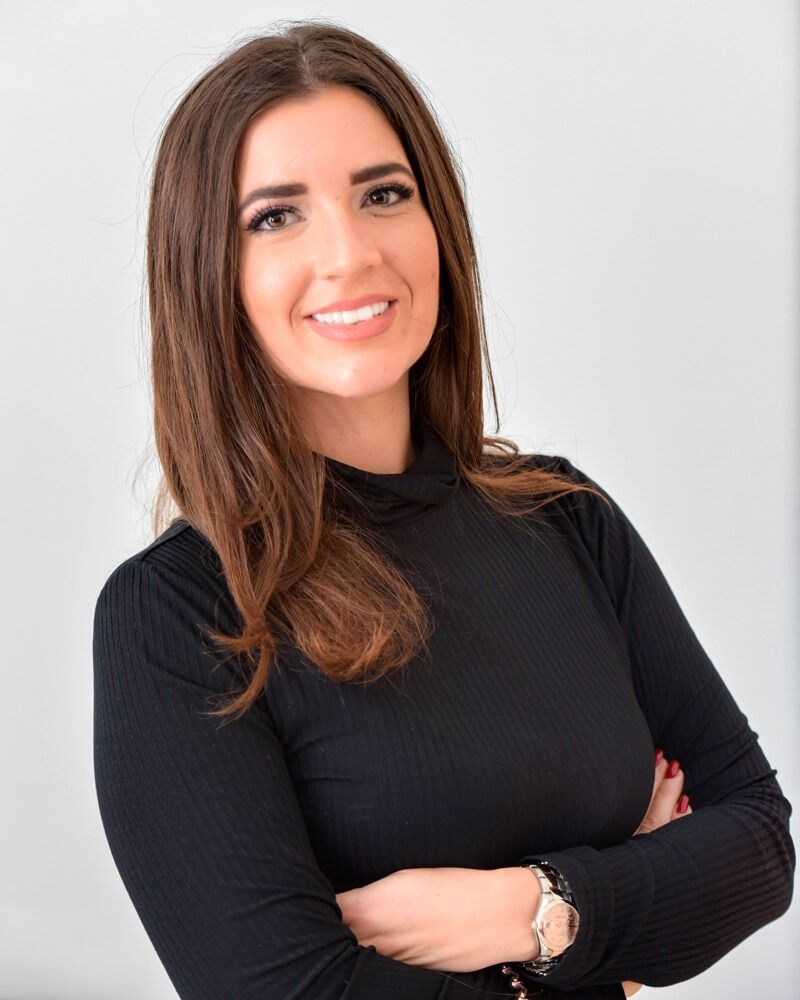 Donna sorridente con top nero e braccia incrociate su sfondo grigio chiaro