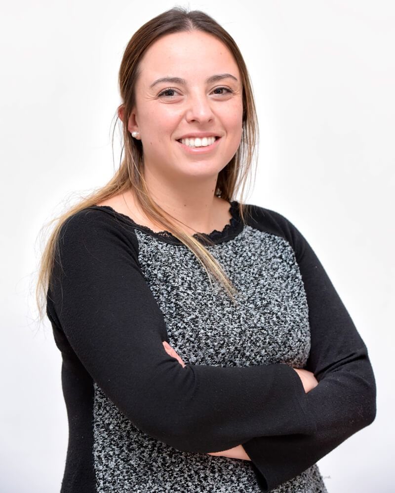 Donna sorridente con le braccia incrociate, con indosso una maglietta nera e grigia, su sfondo bianco.