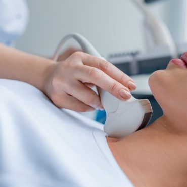 Mano che tiene una sonda ecografica contro il collo di un paziente in una sala visite cliniche
