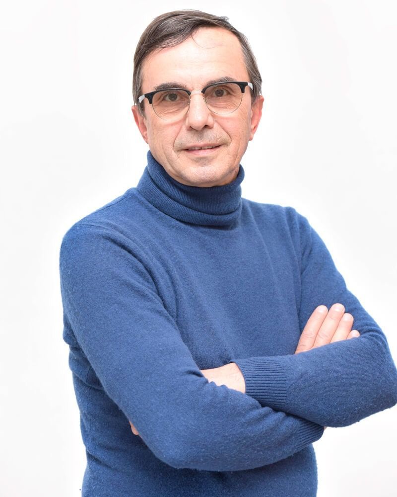 Uomo con maglione blu e occhiali, braccia incrociate su sfondo bianco