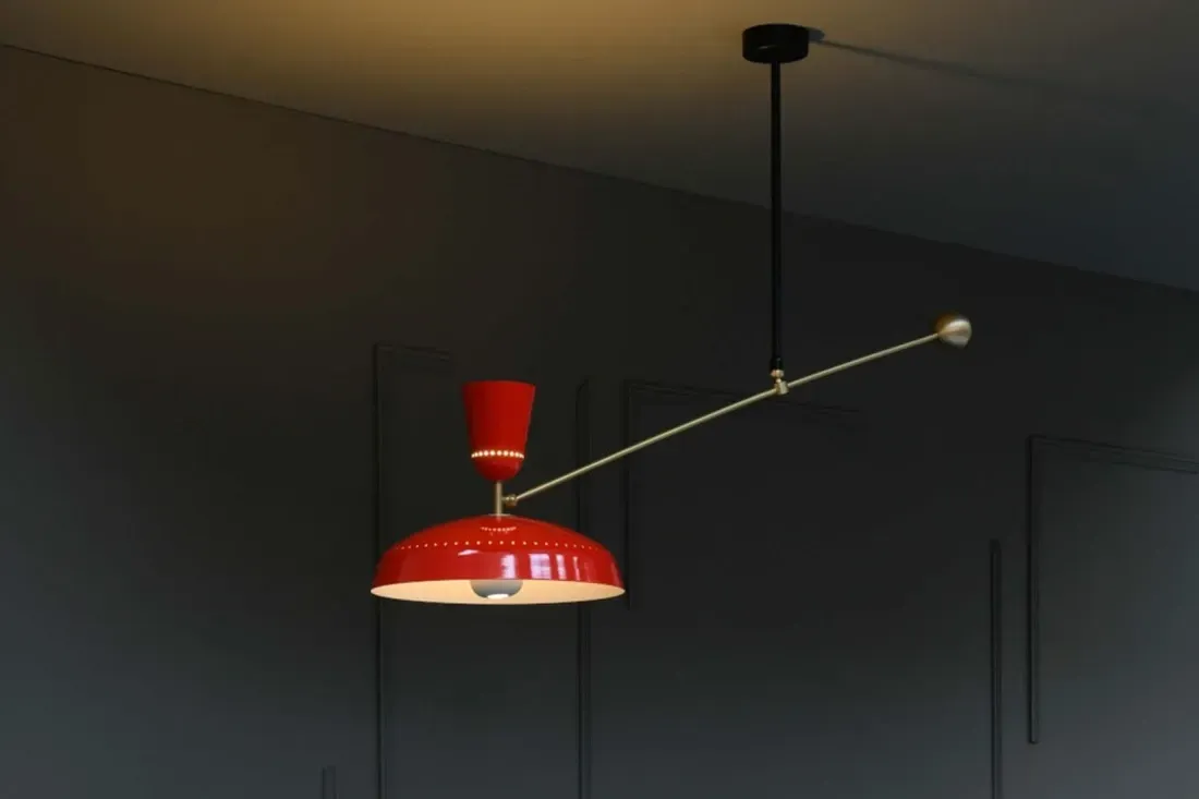 Rød pendellampe hengende fra en svart stang, med en gullfarget arm som strekker seg fra toppen.