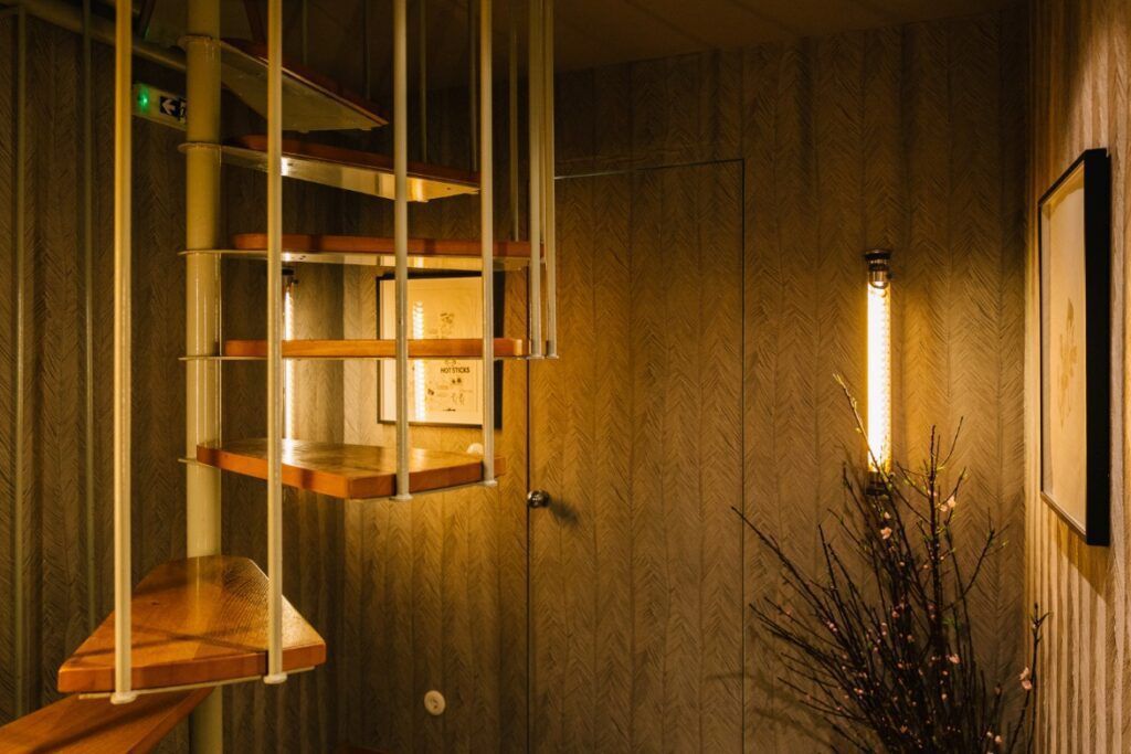 Spiraltrapp med tretrinn, ved siden av en strukturert vegg med et innrammet bilde og en dekorativ lampe.