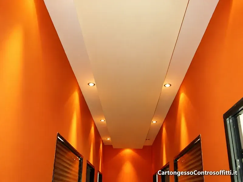 Controsoffitto lineare in cartongesso con faretti in un corridoio dalle pareti arancioni.