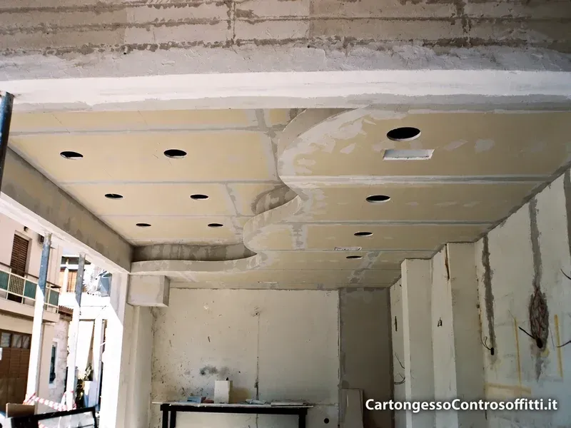 Controsoffitto in cartongesso con fascia curva, giunti stuccati e fori per faretti.
