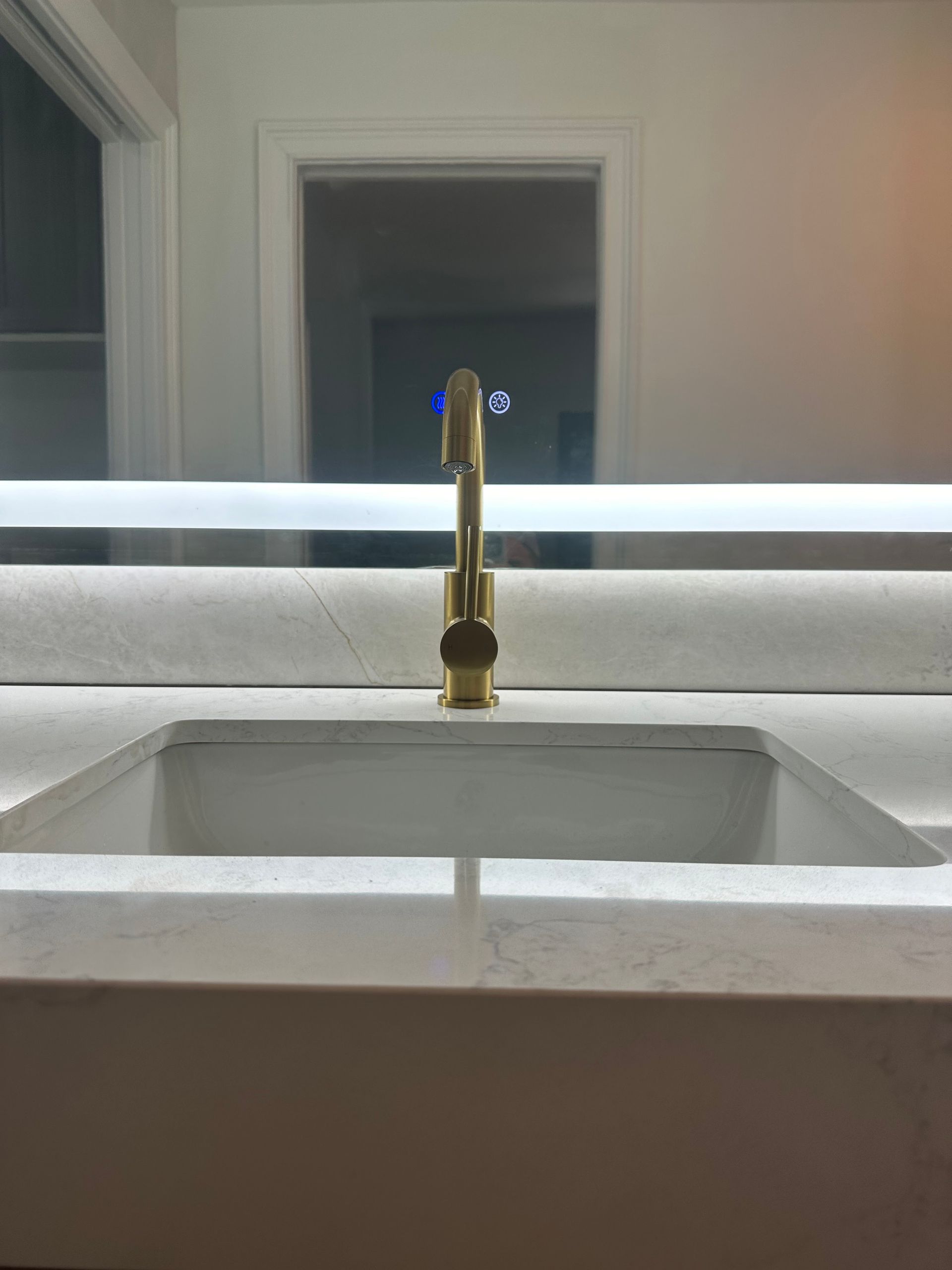 White bathroom sink with a gold faucet beneath a mirror, softly lit at night.
