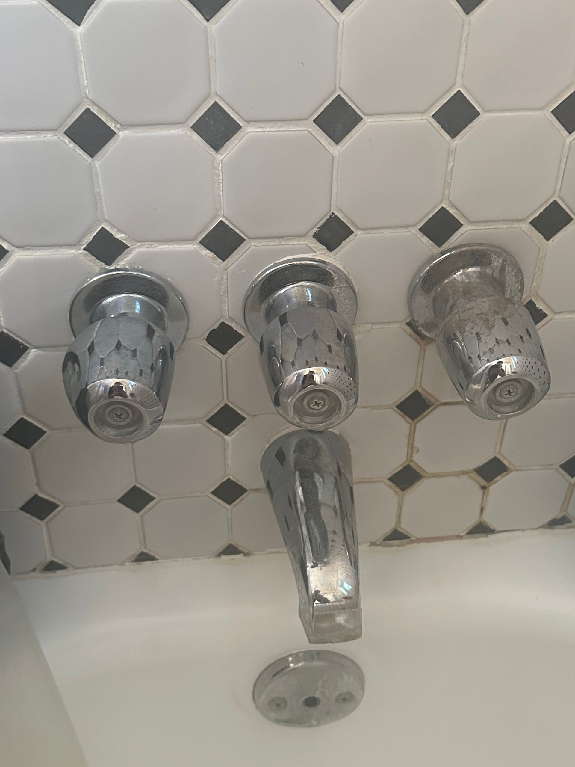Chrome shower knobs and tub spout against white and gray hex tile backsplash