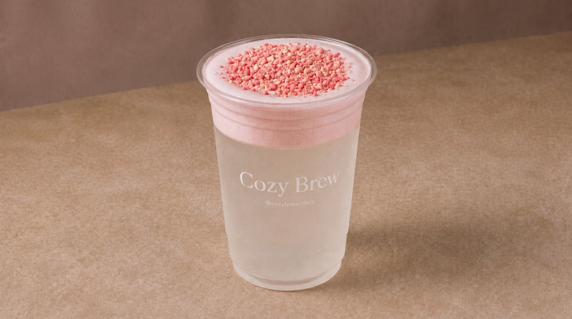 Clear plastic cup with pink foam-topped drink on a tan tabletop