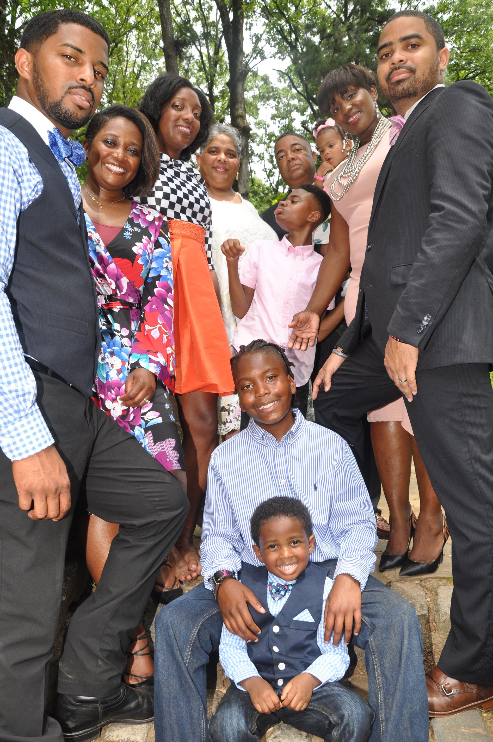 Group of people posing outdoors on steps, with a man in a suit standing beside several others and two children in front.