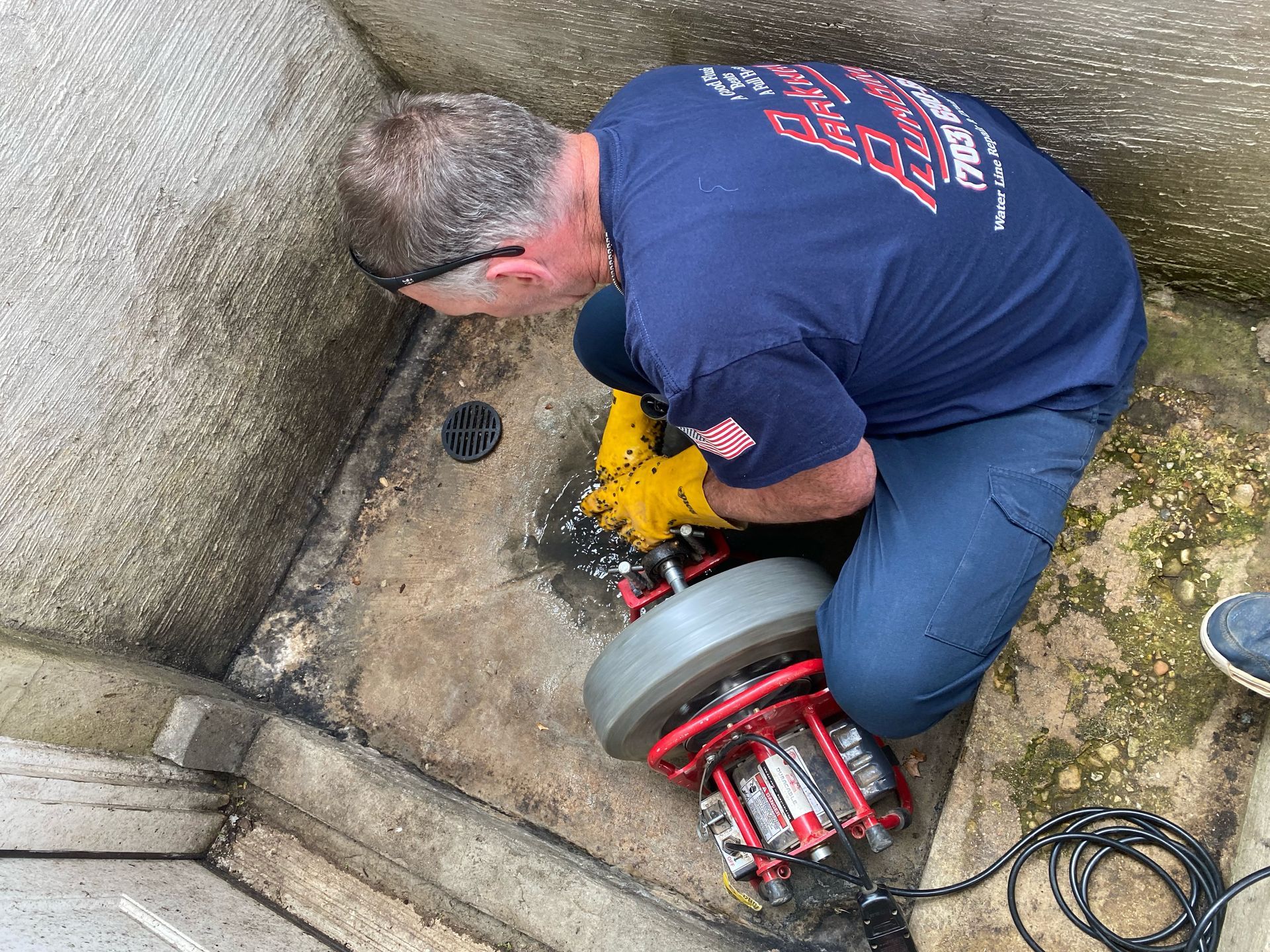 Worker using a drain-cleaning machine in a concrete corner beside a wall and drain opening
