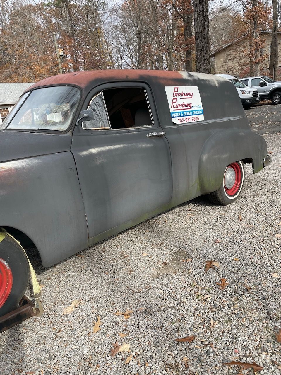 Vintage black coupe with red roof and wheels, parked on gravel with a sign in the side window.