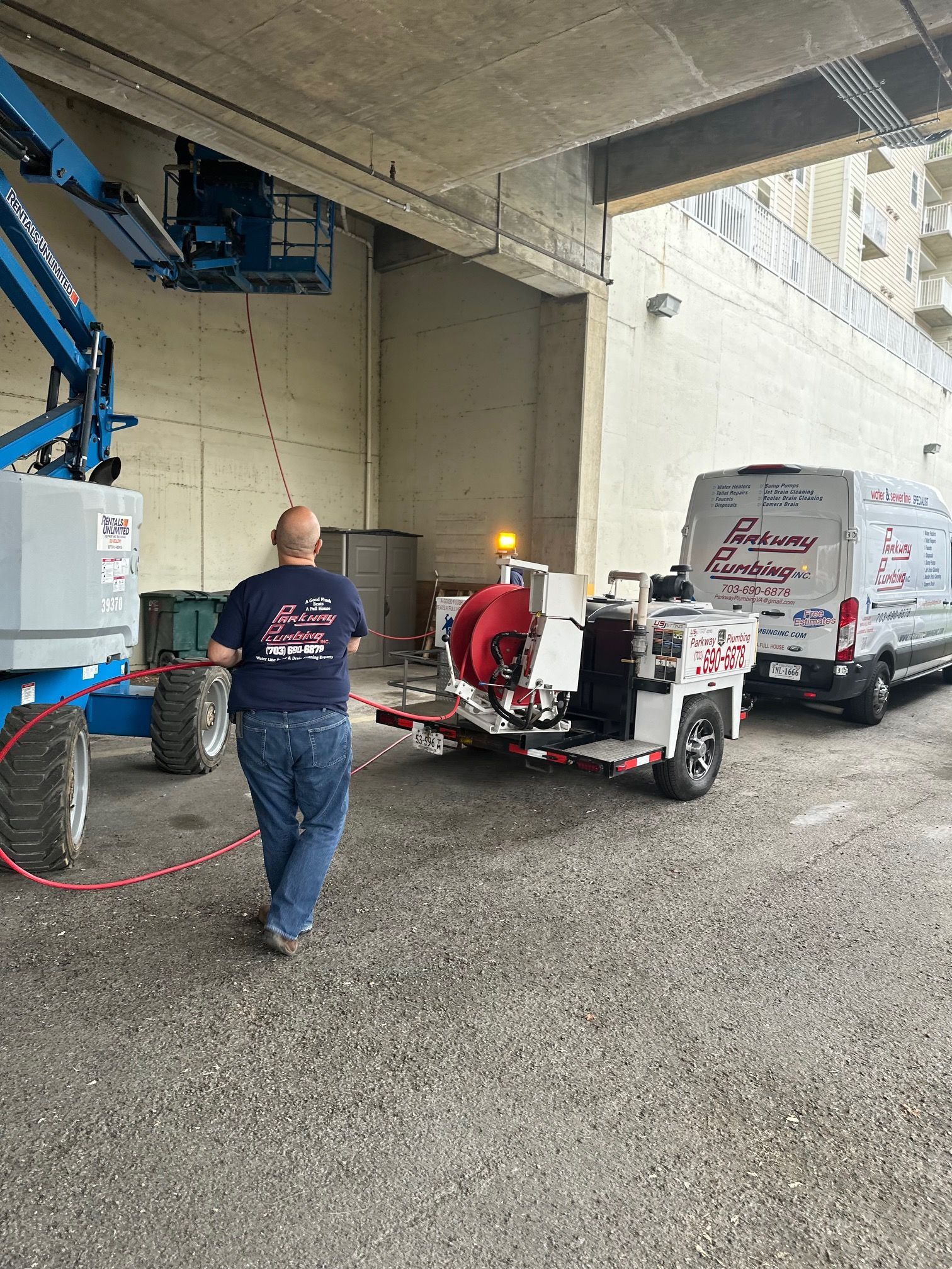 Worker in a covered parking area operating red and white equipment beside service vans and tools