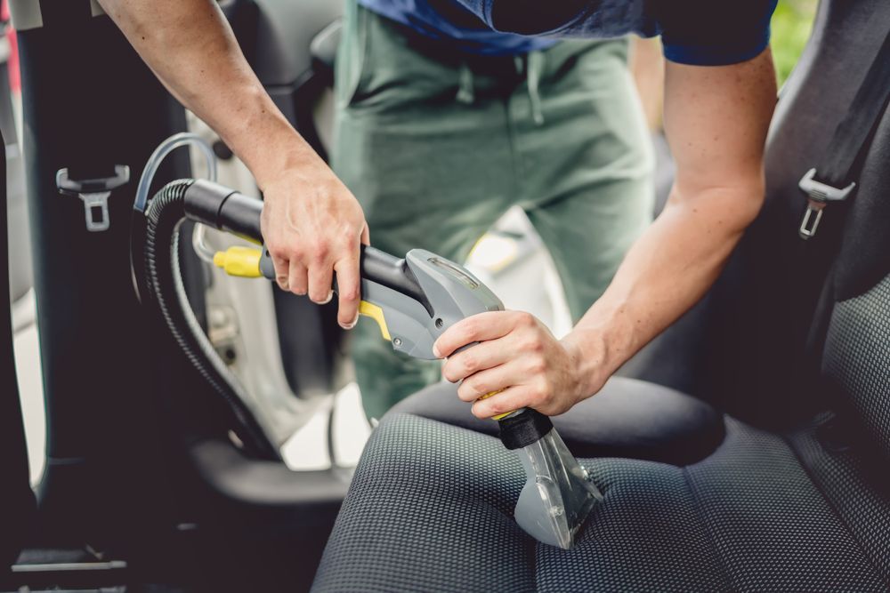A Man Is Kneeling Down To Clean A Car Seat — Townsville Car Care Centre In Aitkenvale, QLD
