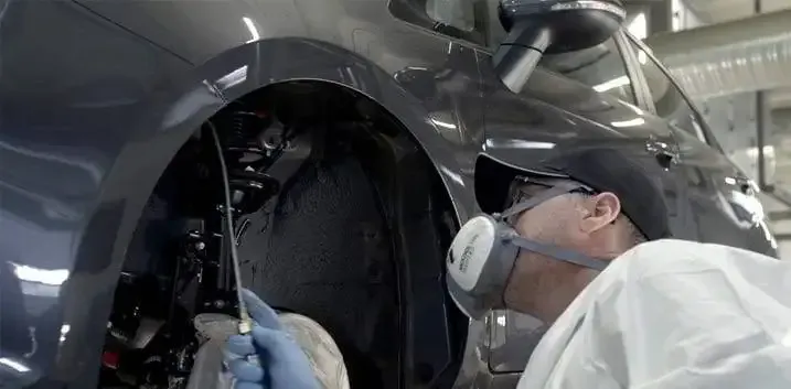 A Man Wearing A Mask Is Working On A Car In A Garage — Townsville Car Care Centre In Aitkenvale, QLD