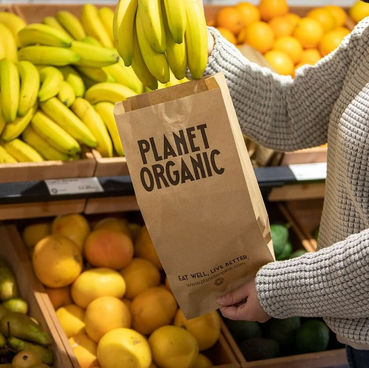 a person is holding a bag that says planet organic with fruit in the background