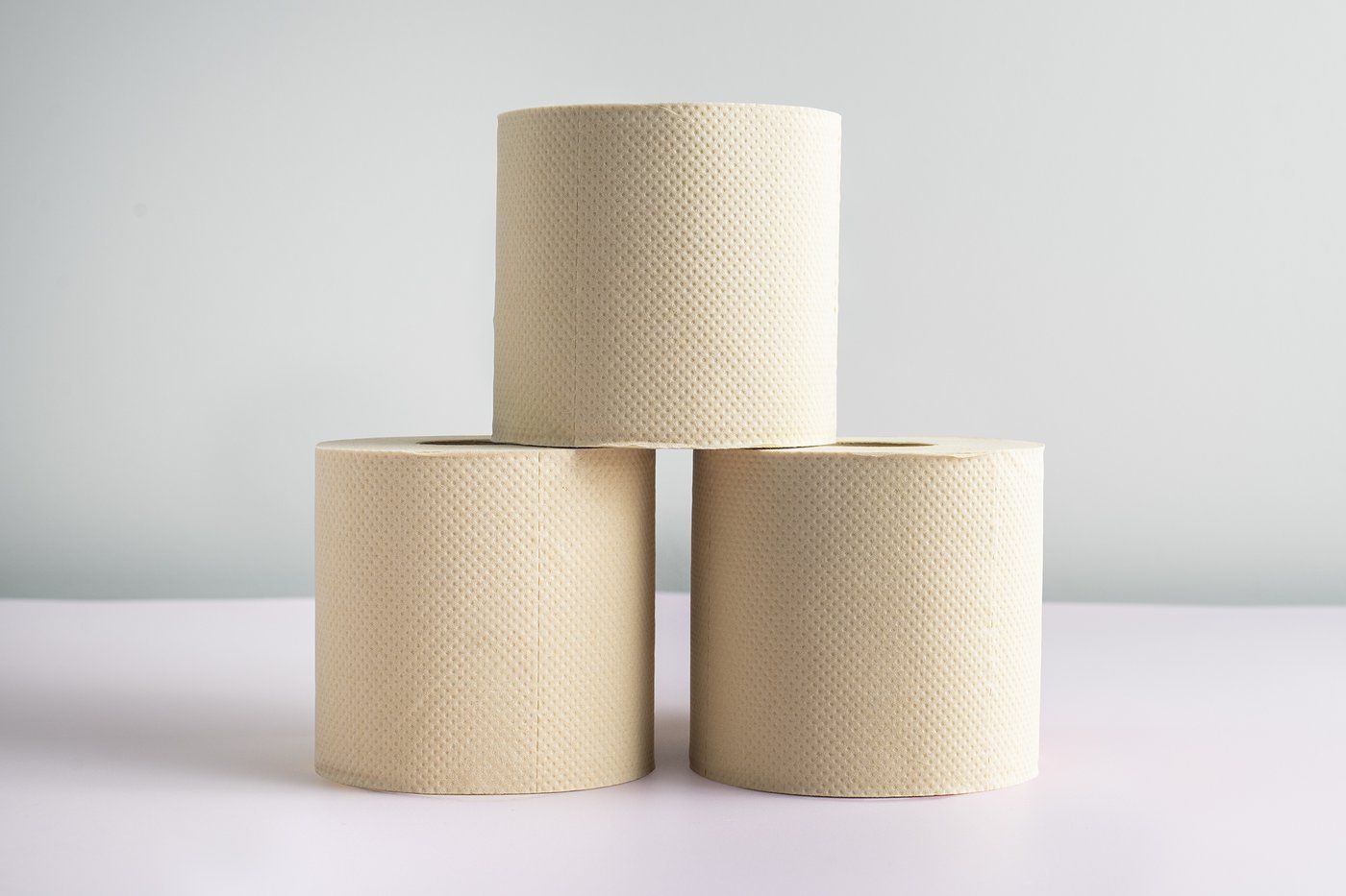 Three rolls of unbleached toilet paper are stacked on top of each other on a table.