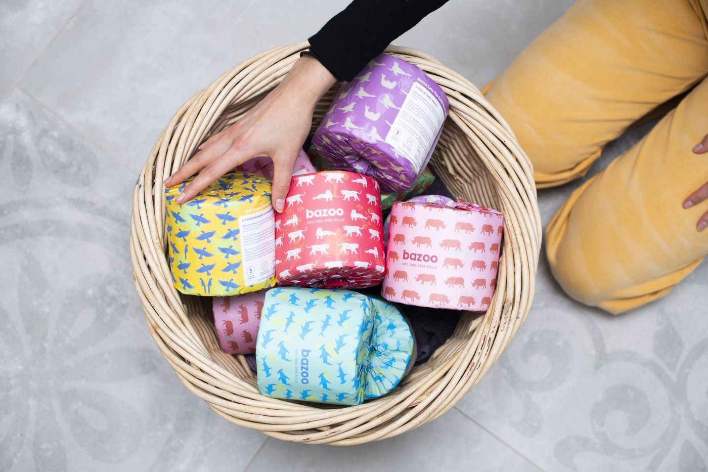 A person is holding a basket filled with rolls of toilet paper.