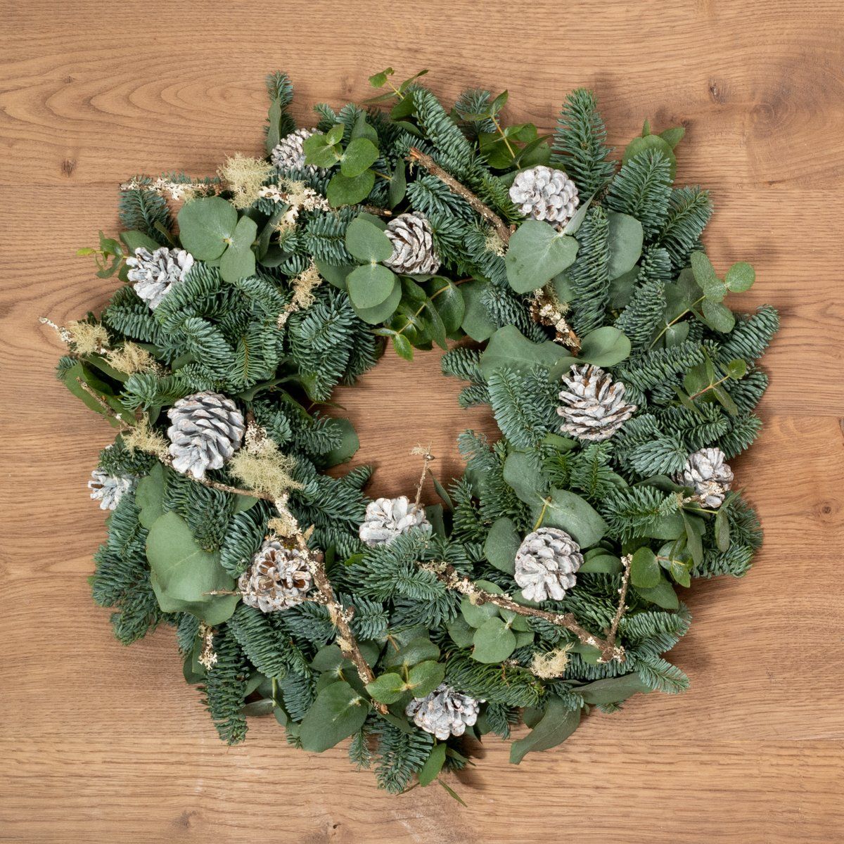 A christmas wreath with pine cones and eucalyptus on a wooden table.