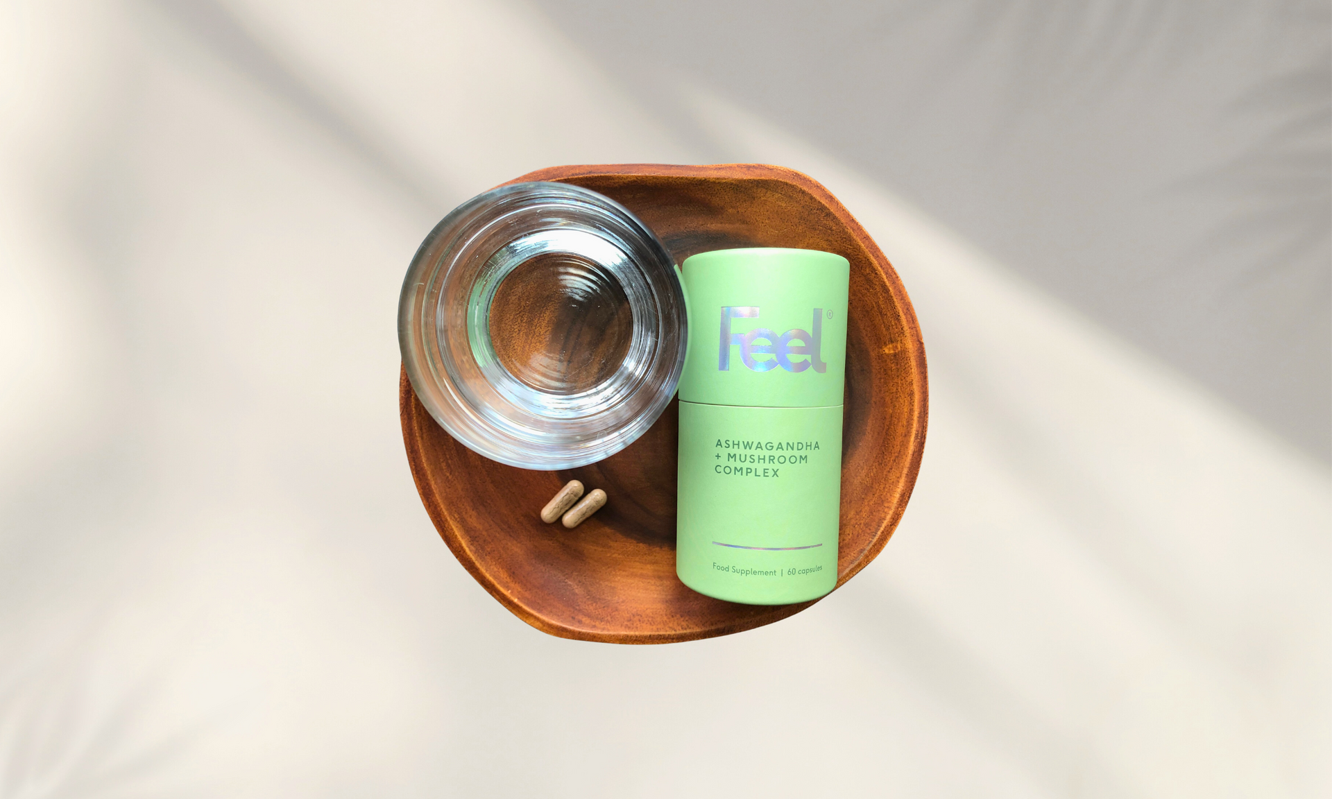 a wooden plate topped with a bottle of Ashwagandha and mushroom supplement capsules and a glass of water .