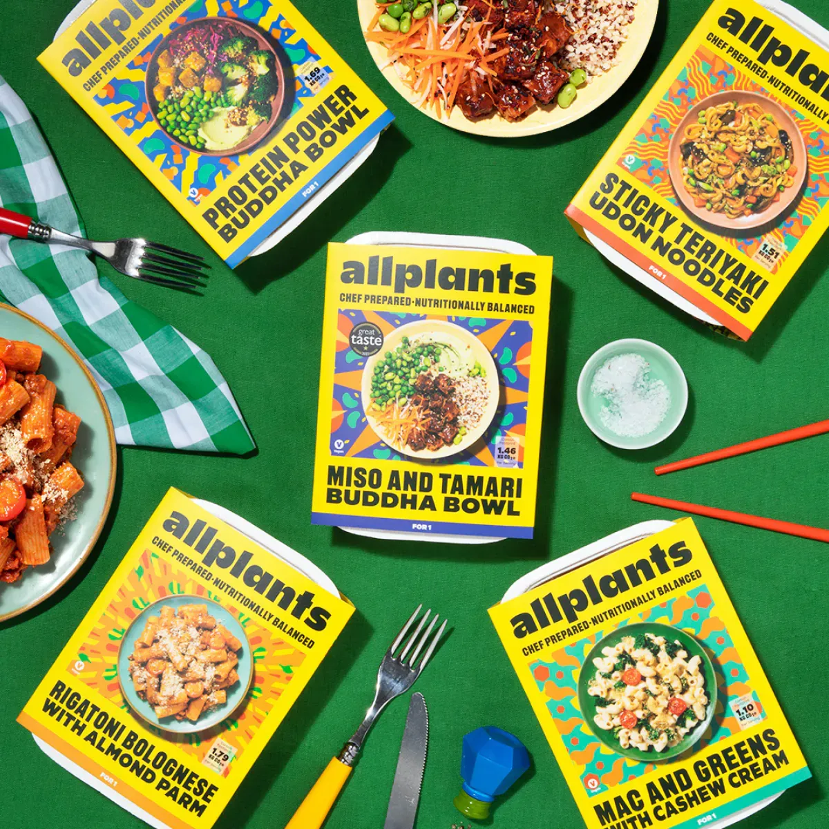 A table topped with plates of food and boxes of allplants noodles.