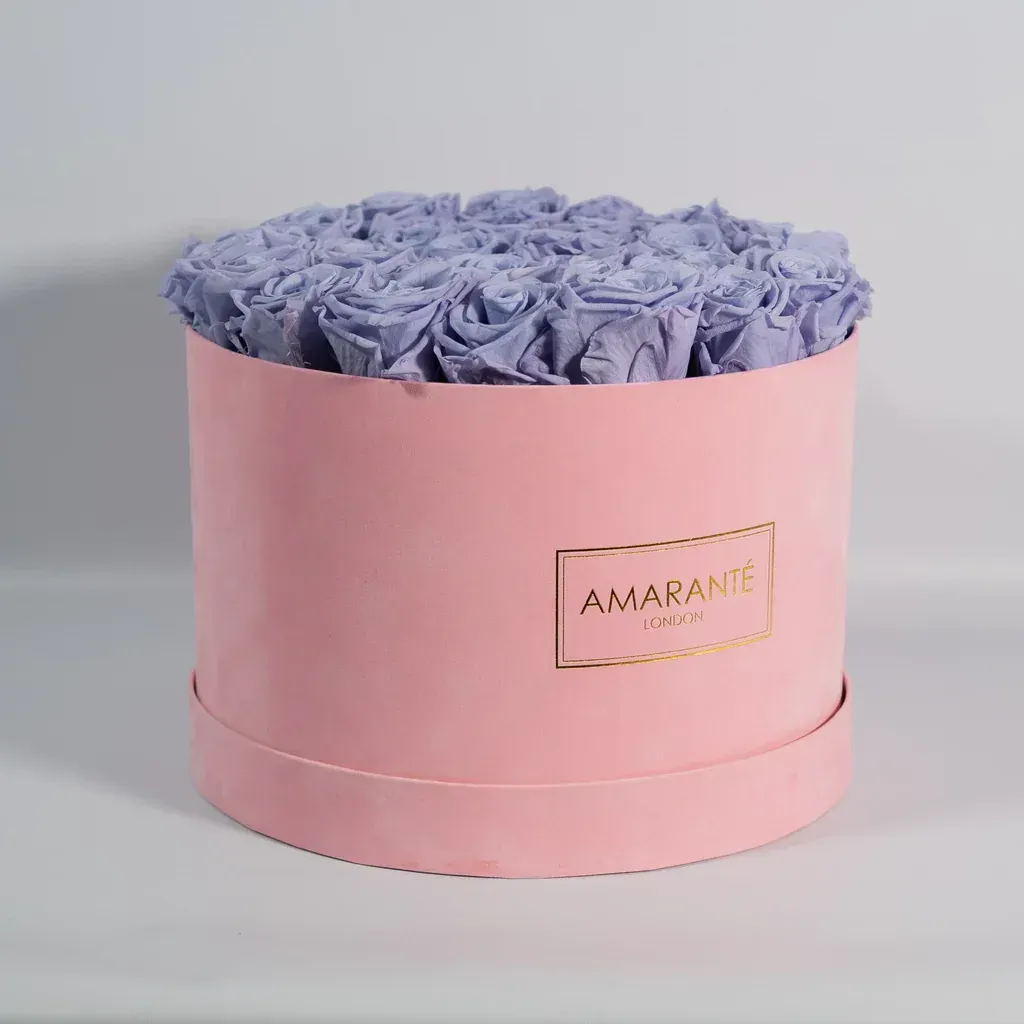 A pink box filled with purple roses is sitting on a table.