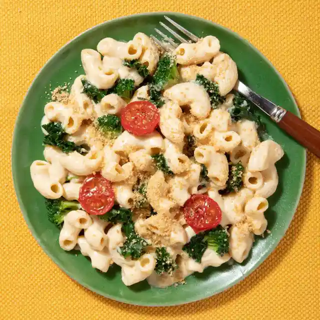 Macaroni and cheese with broccoli and tomatoes on a green plate with a fork