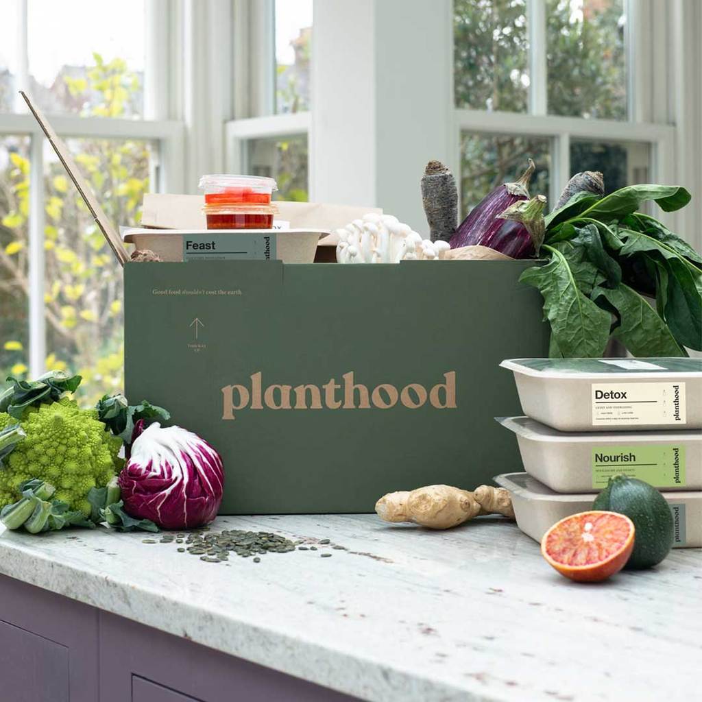 A box filled with vegetables is sitting on a counter next to a window.
