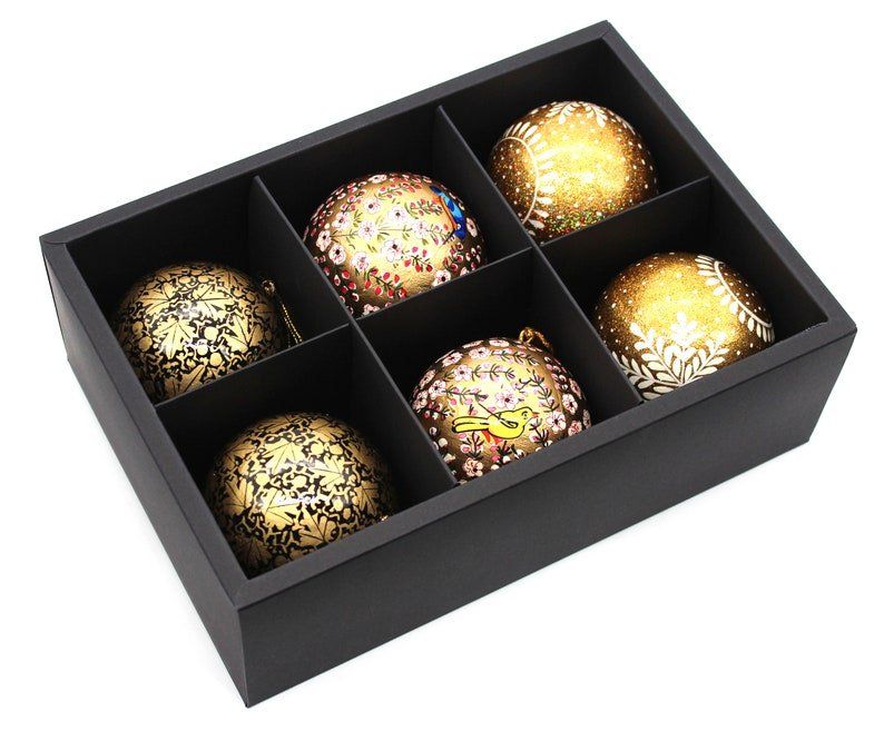 A black box filled with six gold christmas ornaments