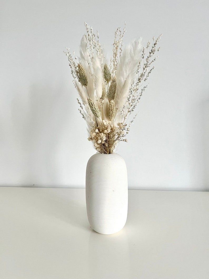 A white vase filled with dried flowers is sitting on a table.