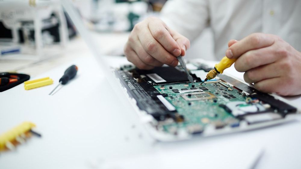a man is working on a laptop with a yellow screwdriver