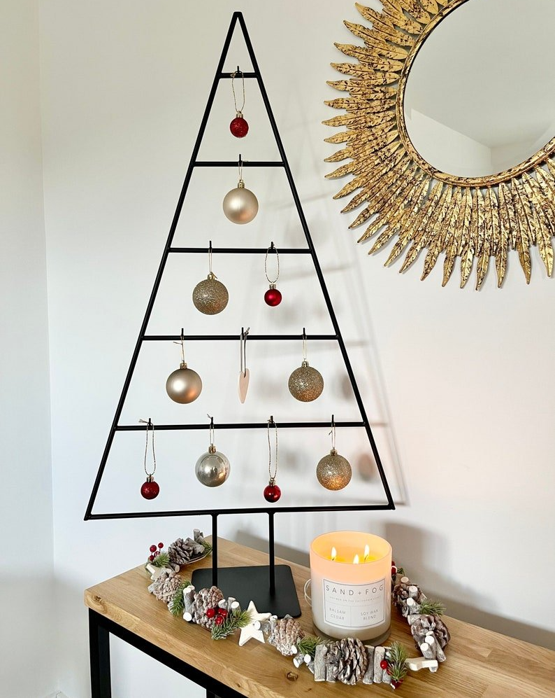 A christmas tree is sitting on a wooden table next to a candle and a mirror.