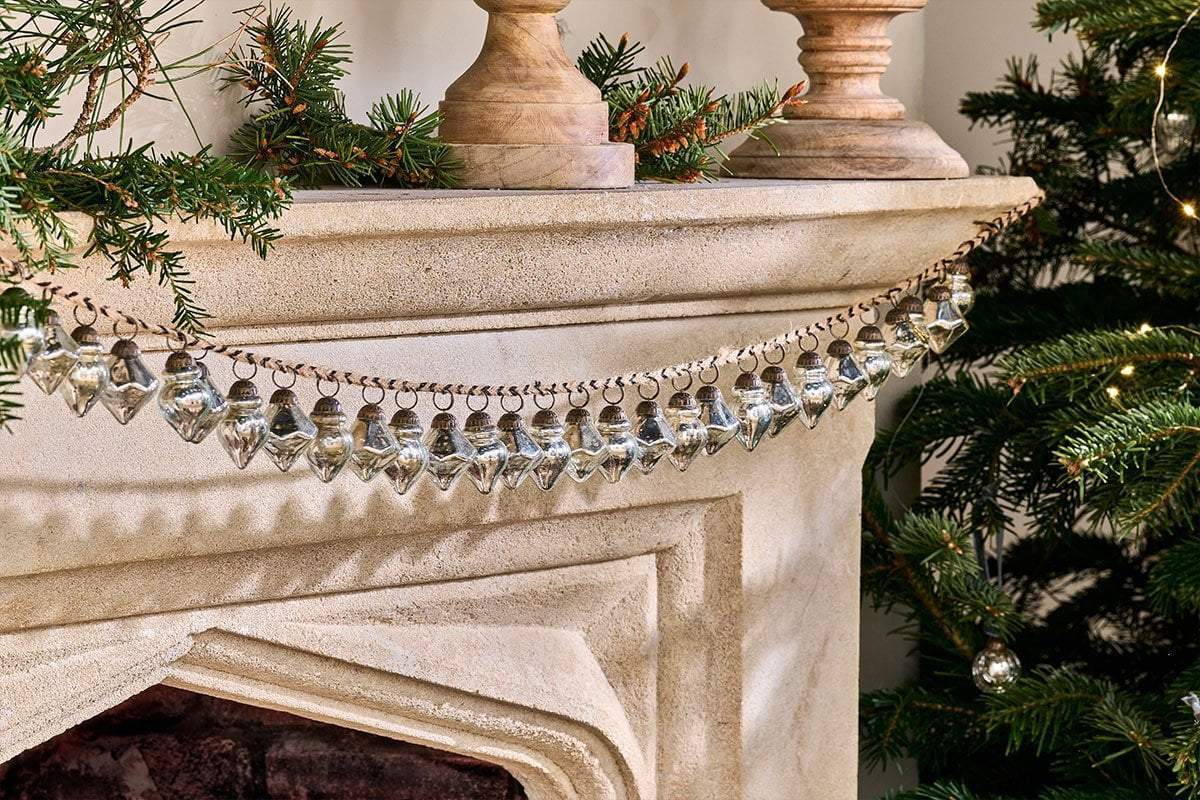 A christmas tree is sitting next to a fireplace with a garland on it.