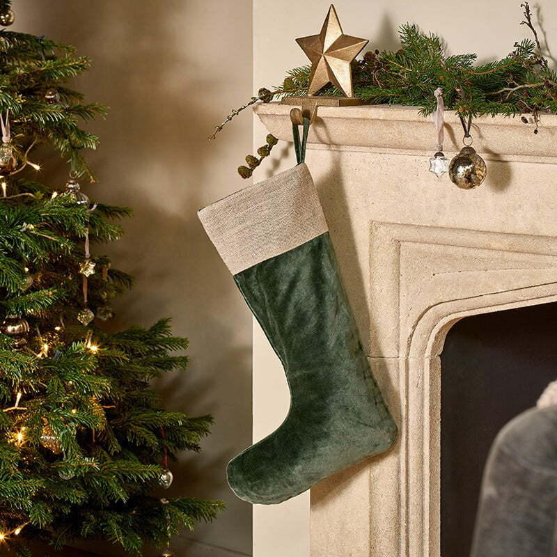 A green christmas stocking hangs on a mantle next to a christmas tree
