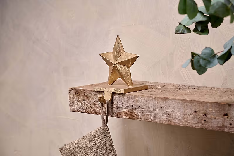 A christmas stocking holder with a star on top of it is sitting on a wooden shelf.
