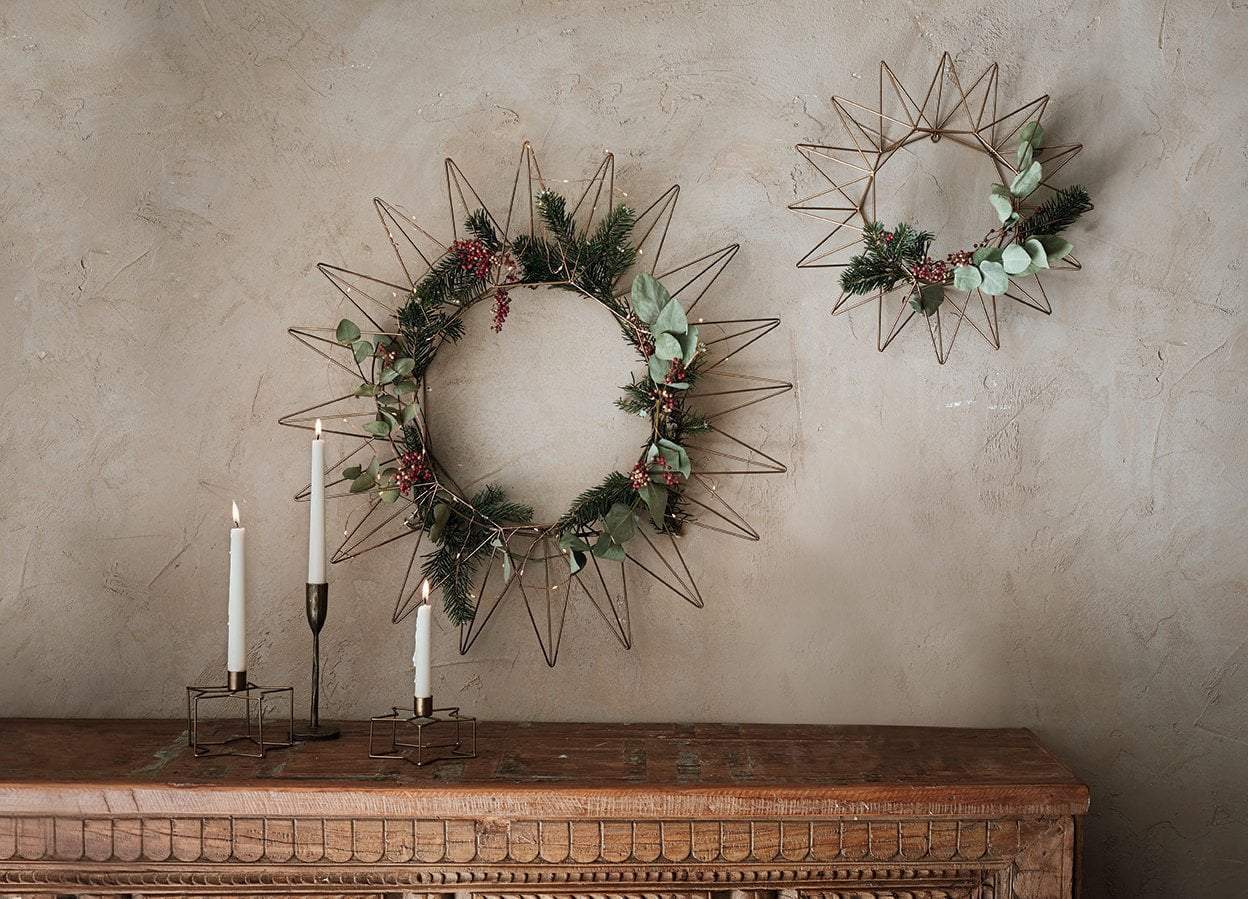 Three wreaths are hanging on a wall next to candles on a table.