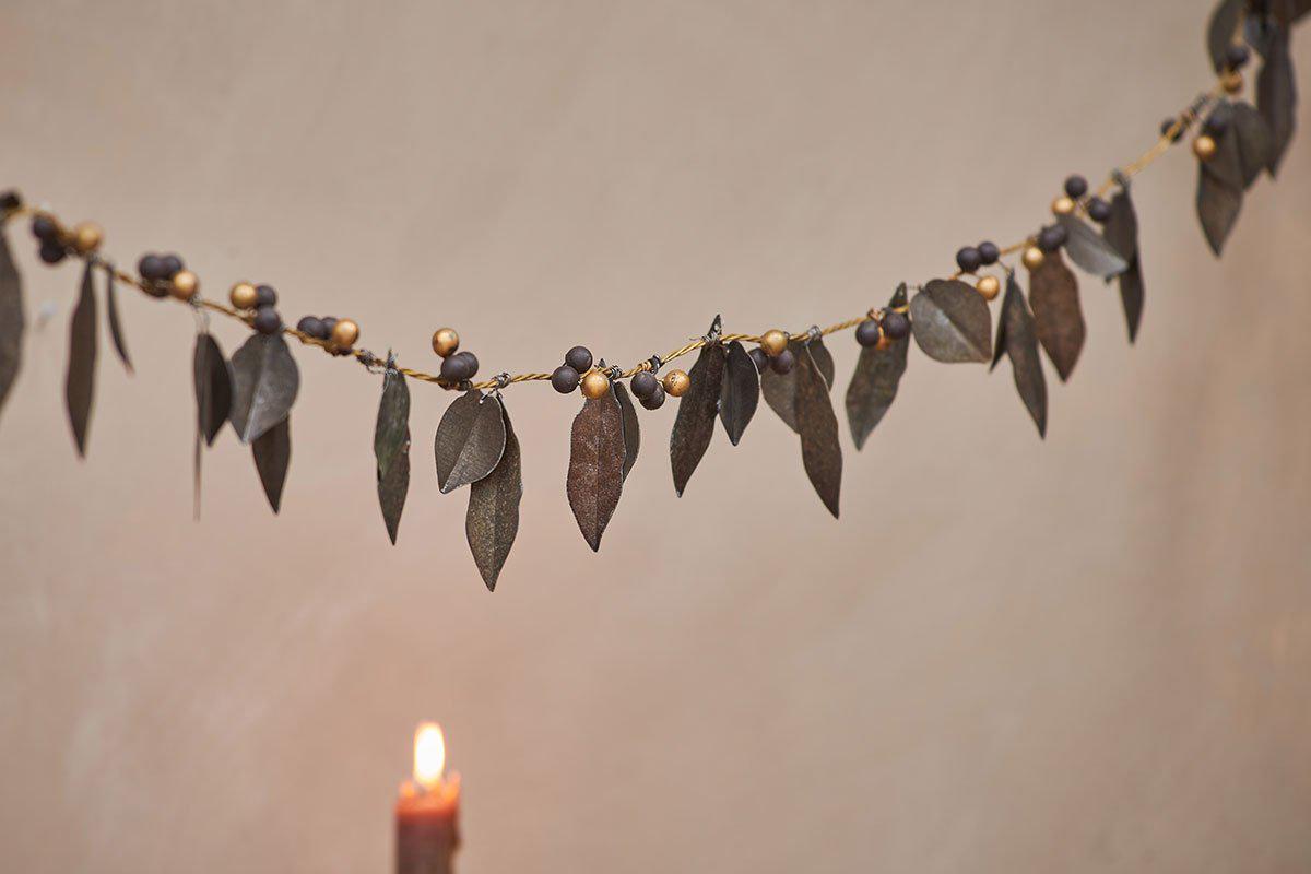 A candle is lit next to a garland of leaves and berries.