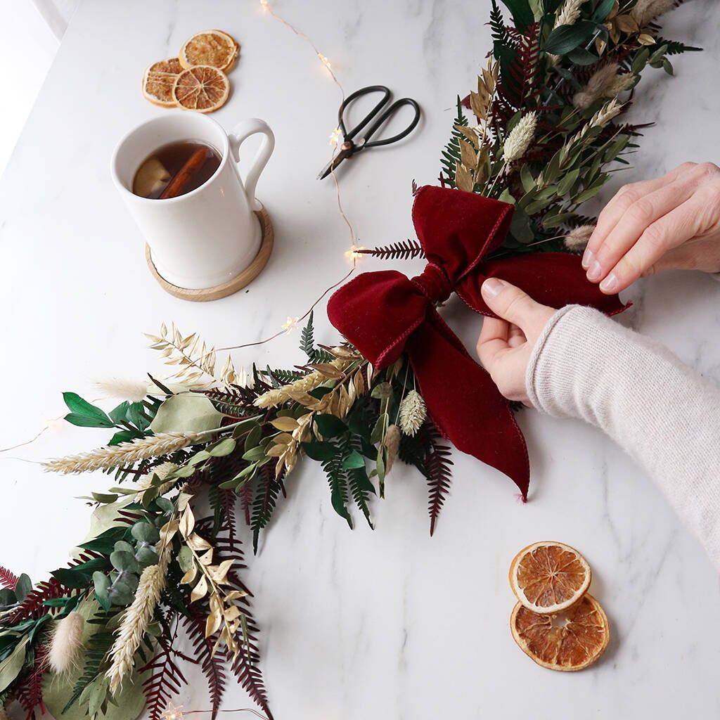 A person is making a christmas wreath with flowers and a red bow.
