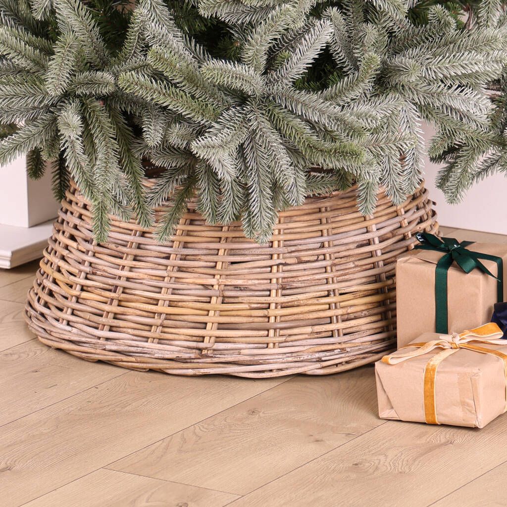 A wicker christmas tree skirt is sitting on a wooden floor next to gifts.