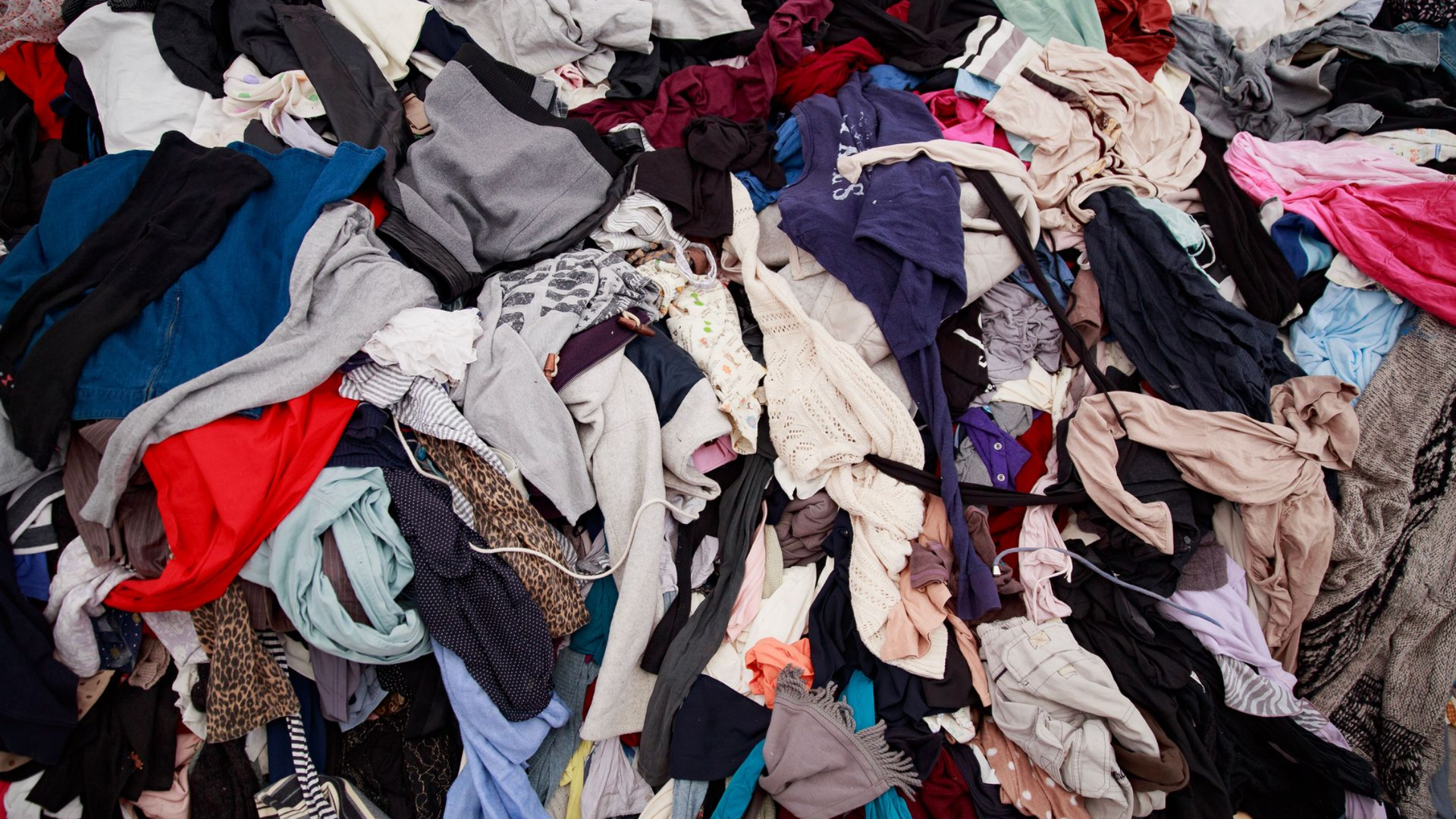 Pile of assorted used clothing in mixed colors, piled together in a heap.