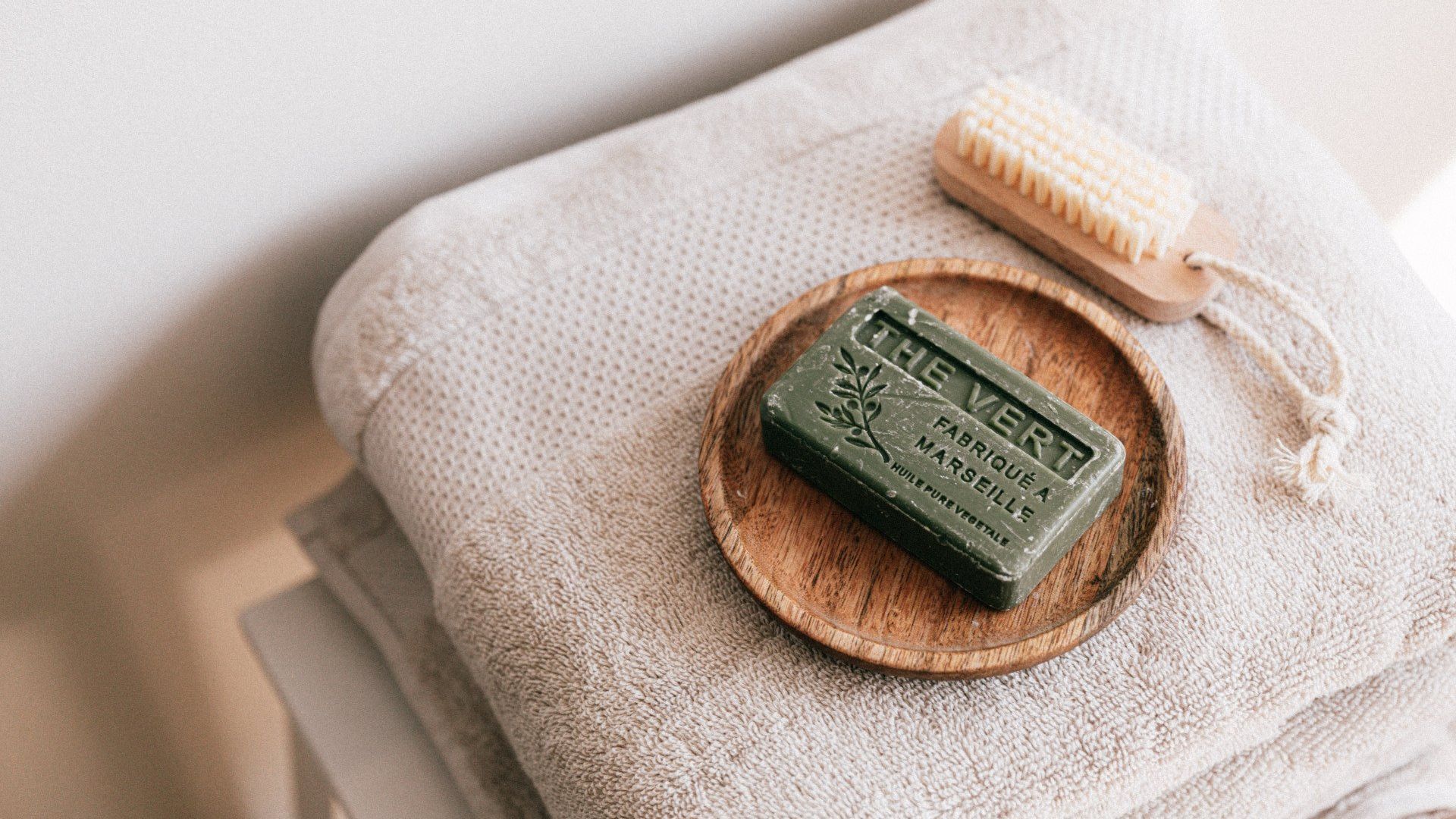 A bar of soap is sitting on top of a stack of towels next to a brush.