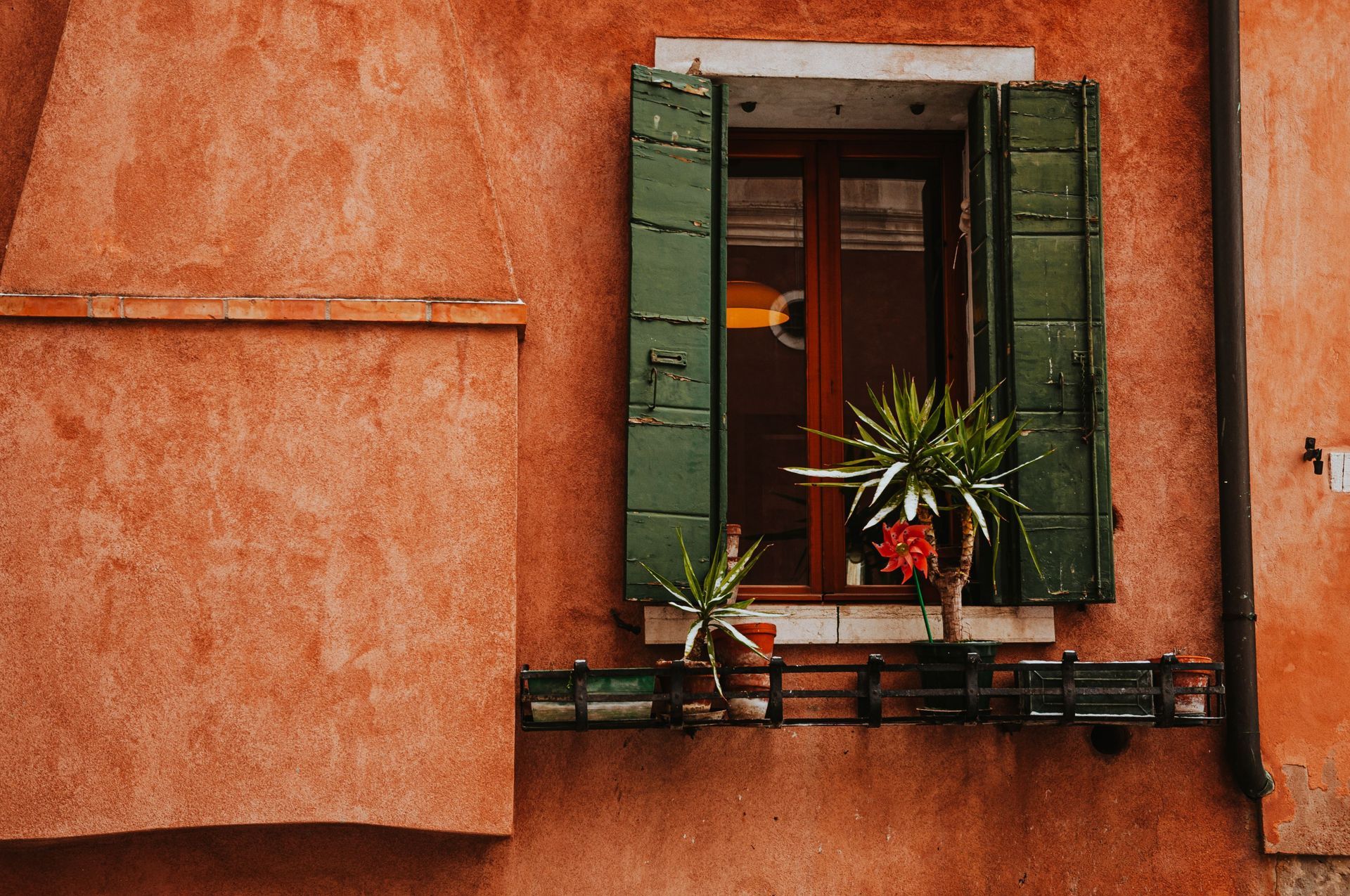 Small window with green shutters and potted plants on an orange stucco wall