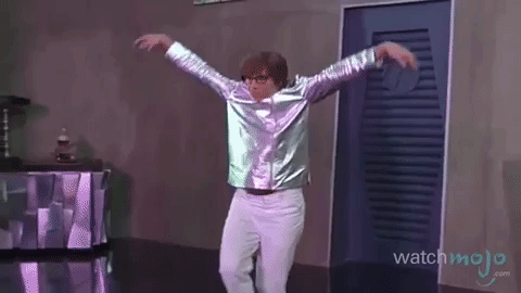 A man in a silver shirt and white pants is dancing in a room.