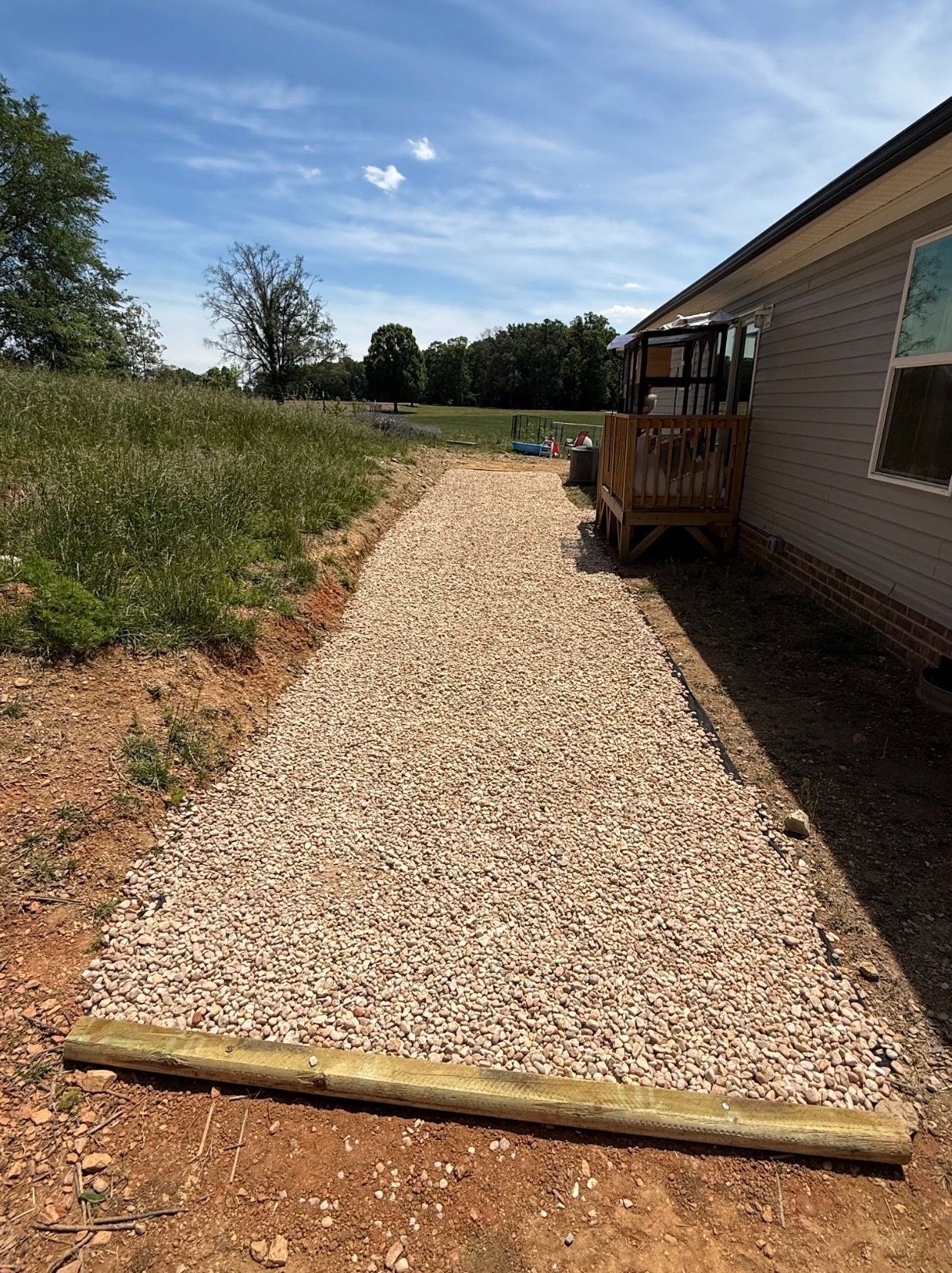 Gravel path beside a house with a wooden ramp, bordered by grass under a blue sky.