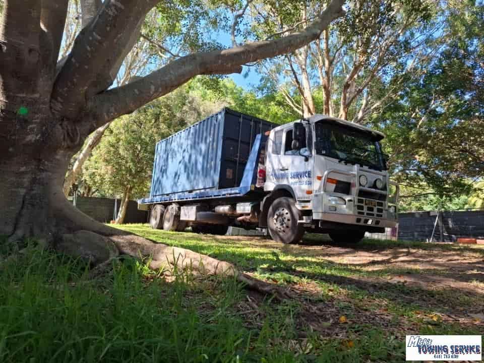 A White Truck with A Blue Container Parked Under a Large Tree on A Grassy Area — Mick's Towing Service Pty Ltd in Carrara, QLD