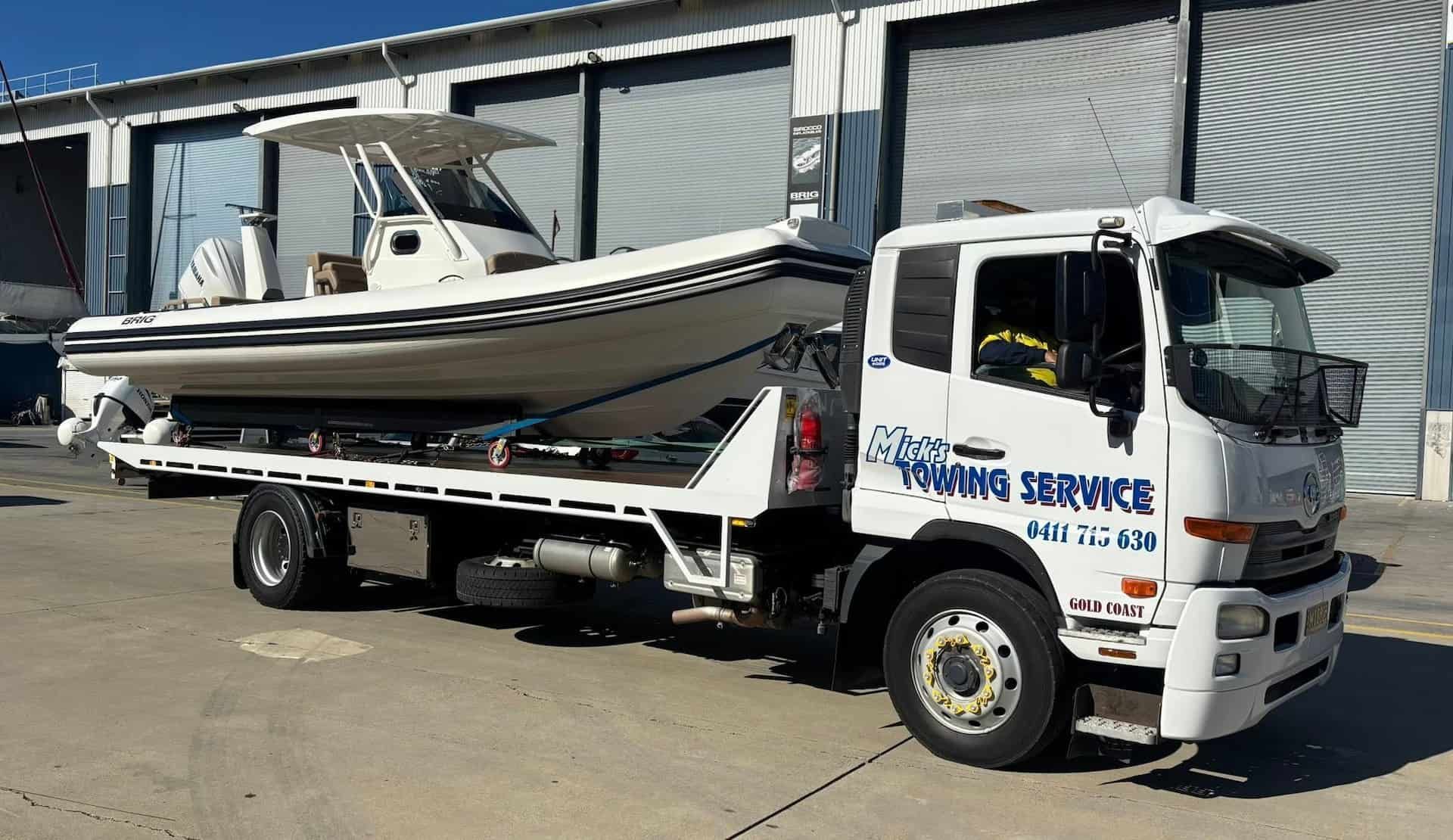 A Tow Truck With a Boat on the Back is Parked in Front of a Building — Mick's Towing Service Pty Ltd in Carrara, QLD