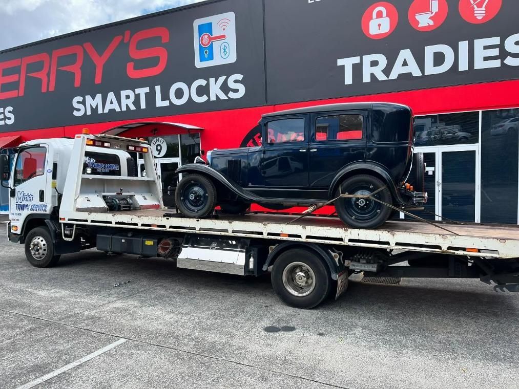 An Old Car Is Being Towed by A Tow Truck — Mick's Towing Service Pty Ltd in Carrara, QLD