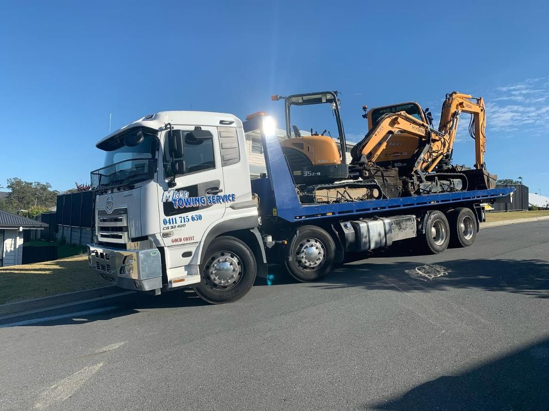 A Tow Truck Is Carrying an Excavator on The Back of It — Mick's Towing Service Pty Ltd in Carrara, QLD